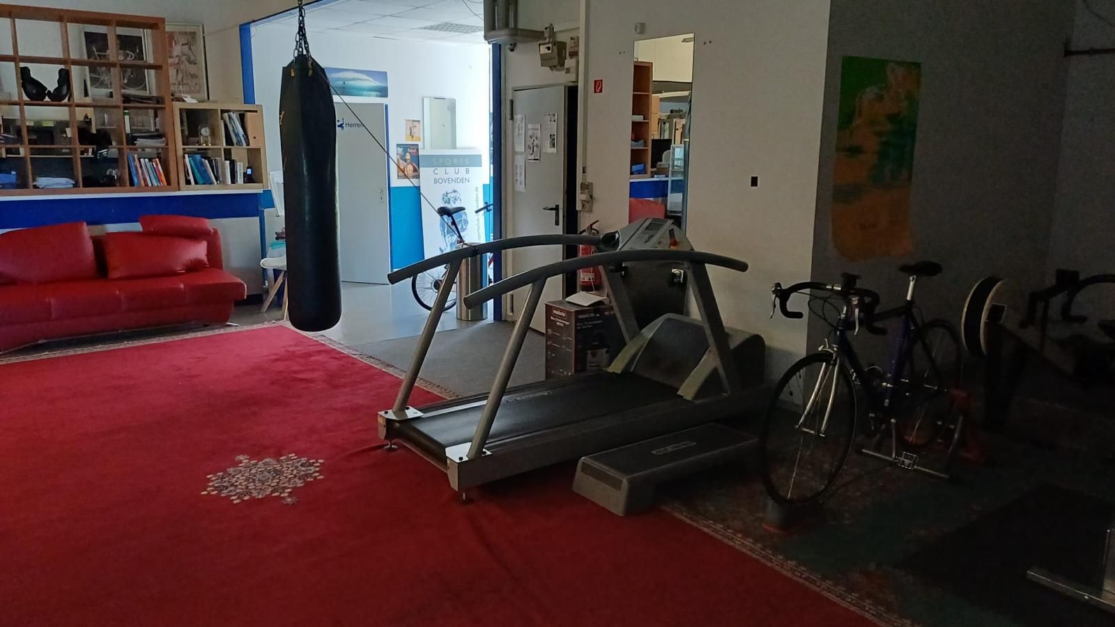 Gemütliche Sitzecke mit rotem Sofa, Cardiogeräten und Studio-Eingang